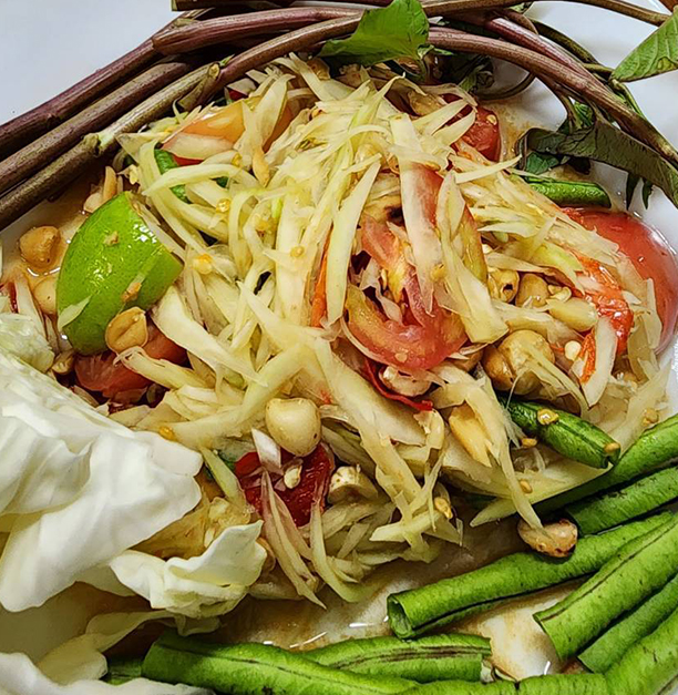 Traditional Thai papaya salad served in a woven basket with fresh vegetables