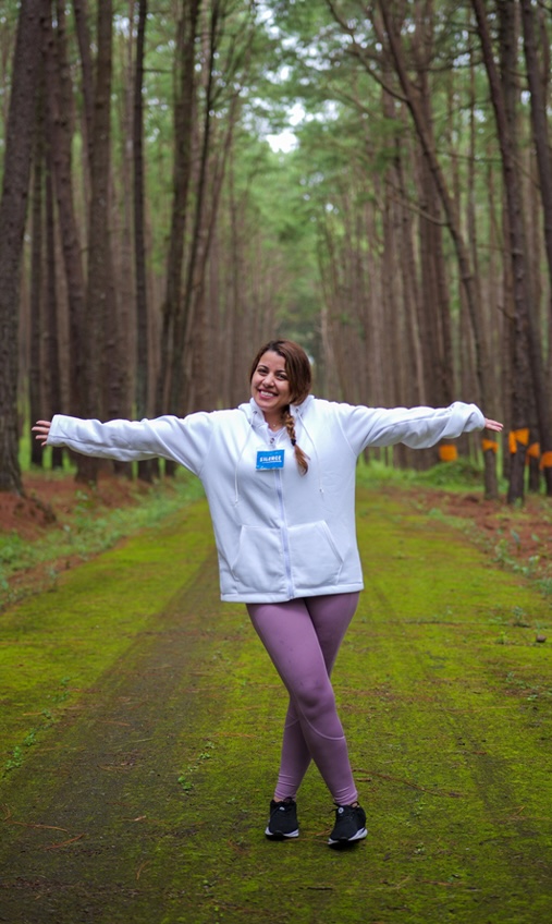 Woman in white hoodie with arms spread wide in a peaceful forest setting